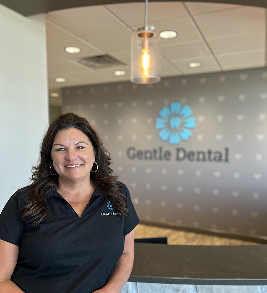 A woman standing in front of a sign for Gentle Dental, posing with a smile.