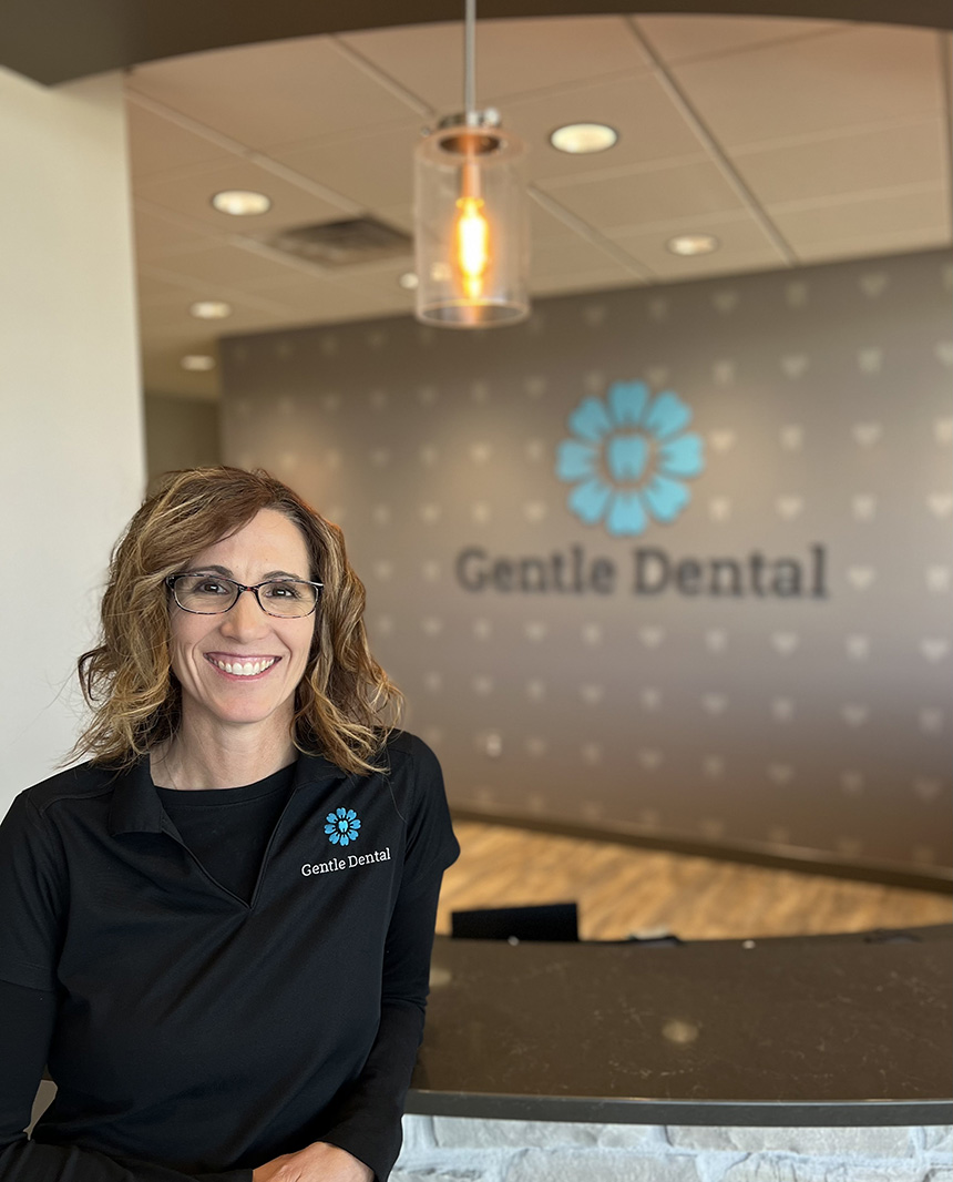 A woman standing in front of a sign for  Gentle Dental  in an office setting.