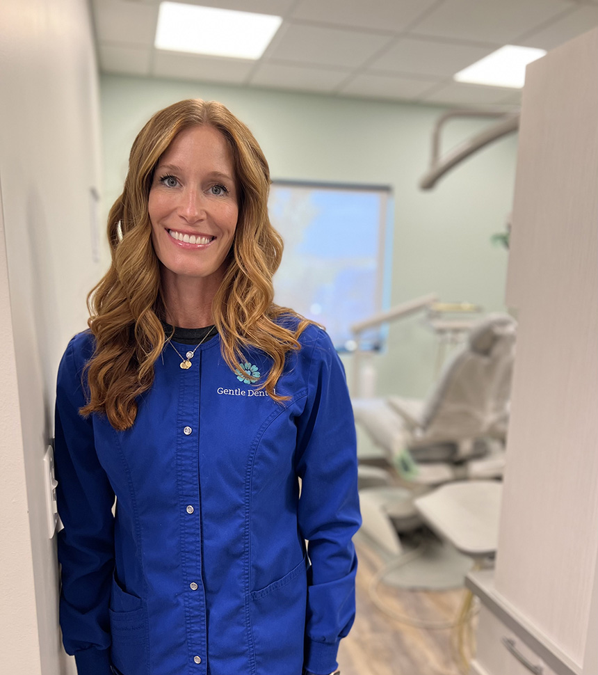 A woman standing in a dental office, smiling at the camera.