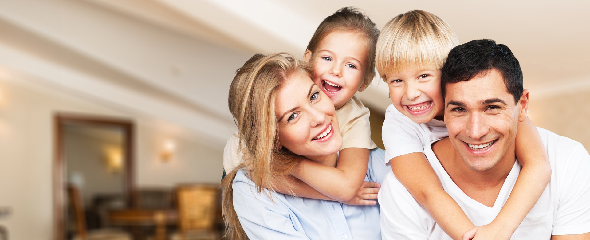 A happy family posing together with smiles, consisting of two adults and three children, in a home setting.
