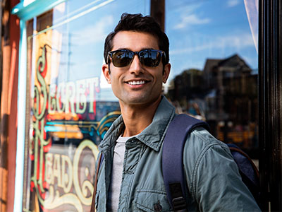 A man wearing sunglasses stands outside a storefront, posing with a backpack.