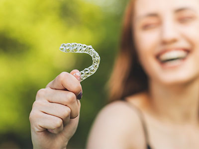 The image shows a person holding up a toothbrush with a smiley face design, suggesting dental hygiene and a playful approach to oral care.