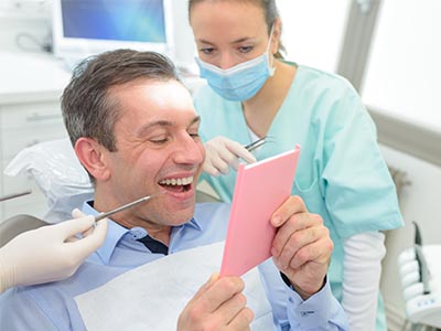 This is a split-screen photograph featuring two different scenes  on the left, a man with a smile, holding a pink card, appears to be in a dental office setting with medical equipment and personnel  on the right, another scene shows a smiling woman looking at the same card while seated in a dental chair, surrounded by dental tools.