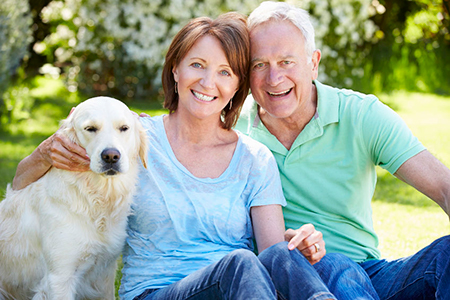 An elderly couple with their golden retriever dog sitting between them outdoors.