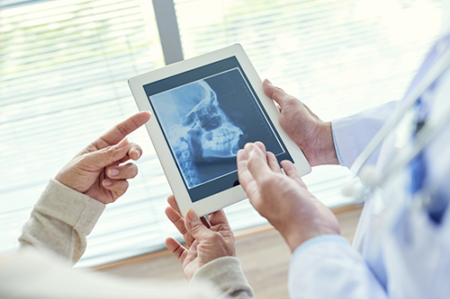 The image shows two individuals interacting with a tablet displaying an X-ray, with one person holding the tablet while another looks at it, suggesting a medical or diagnostic context.
