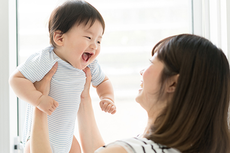 A woman holding a baby while they both laugh, with a blurred background suggesting an indoor setting.