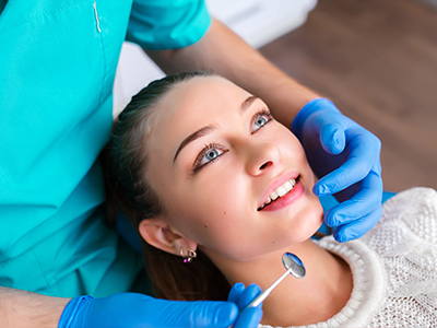 A smiling woman receiving dental care from a professional wearing protective gloves and a face mask.