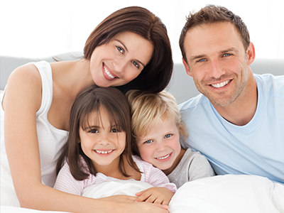 A family of four with two adults and two children posing together on a bed for a portrait.