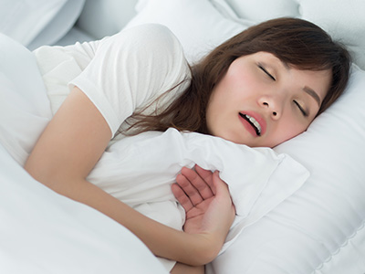 A woman sleeping peacefully with her eyes closed in a bed with white sheets.
