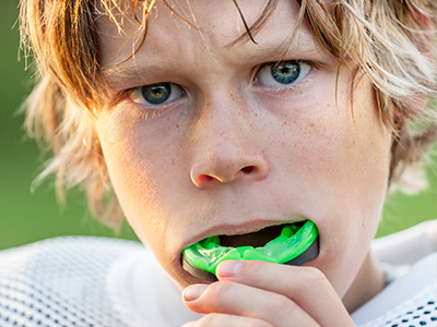 The image shows two photographs of a young boy with blonde hair holding a green object close to his mouth, with the top photo showing him looking directly at the camera and the bottom one showing him from a side angle while chewing on the object.