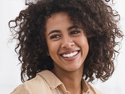 The image features a person with curly hair smiling at the camera, set against a blurred background.